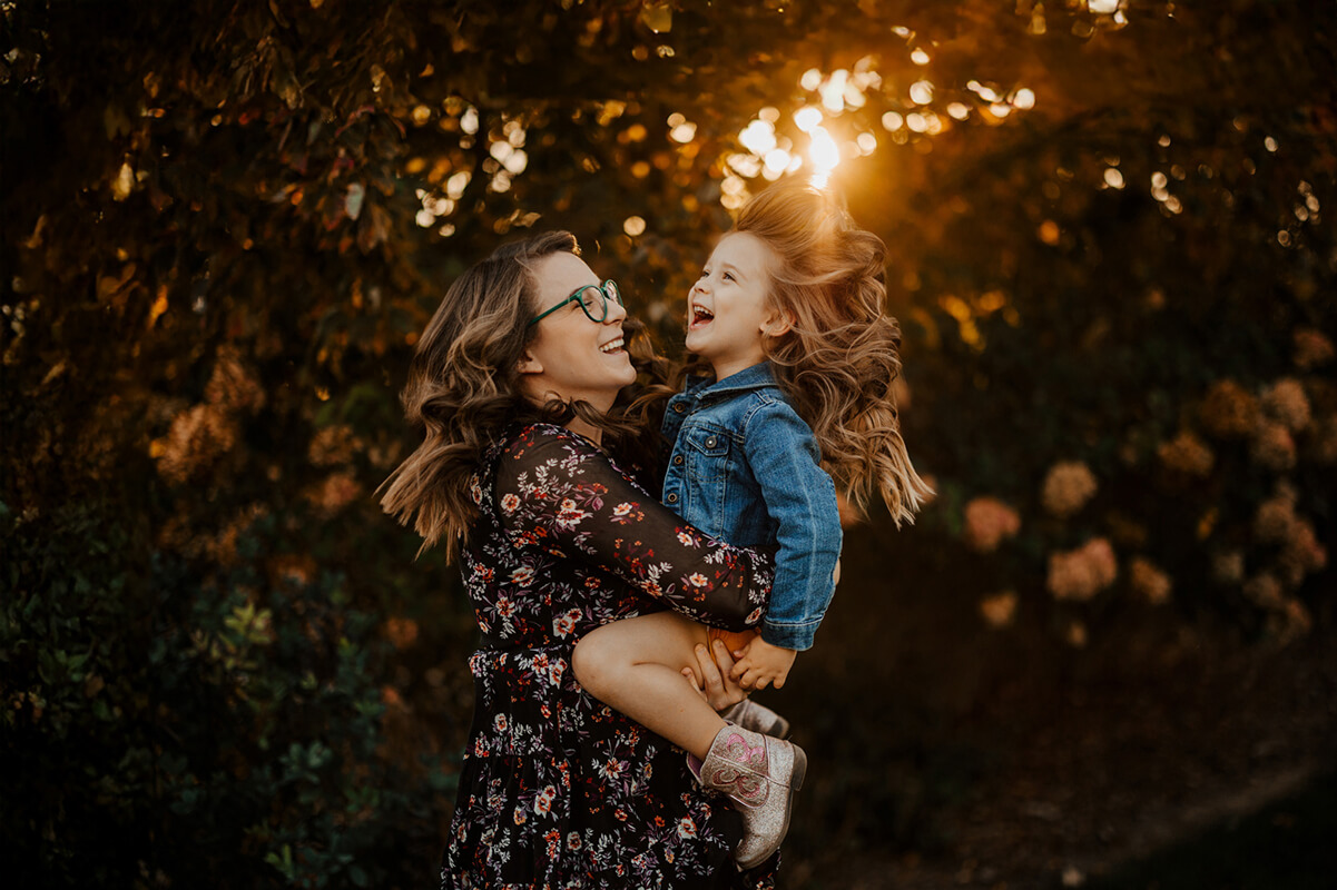 Mother holding laughing daughter at golden hour during candid family photography session West Michigan GAUPERfamilies