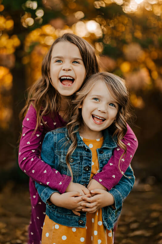 Two sisters laughing and hugging at golden hour during West Michigan family photography session by GAUPERfamilies