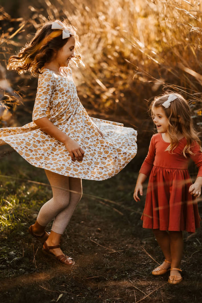 Two little girls twirling in dresses at golden hour during candid family photography session Ludington Michigan