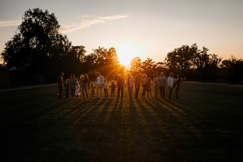 Large extended family holding hands at golden hour sunset during West Michigan family photography session GAUPERfamilies
