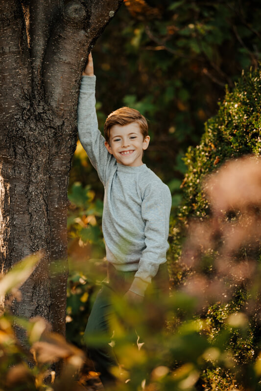 Young boy smiling while climbing a tree during candid extended family photography session Grand Rapids Michigan