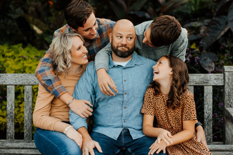 Family of five laughing together on a bench during candid family photography session best West Michigan family photographer