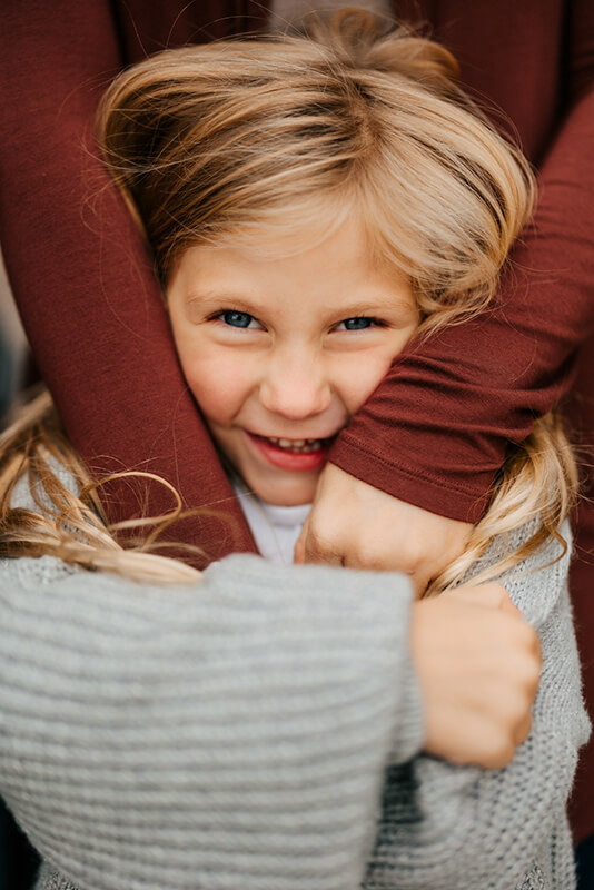 Young child laughing while being hugged from behind during candid family photography session Muskegon Michigan