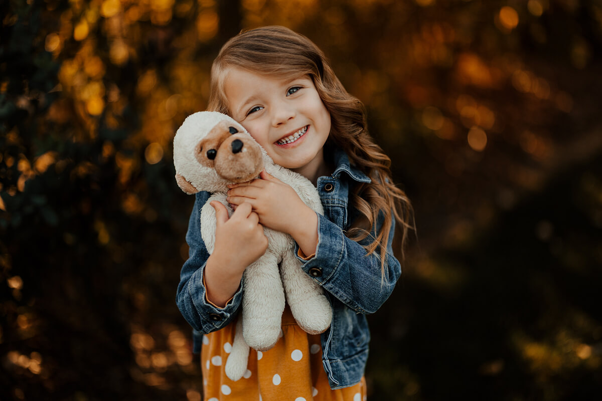 Young girl hugging stuffed animal smiling at golden hour during candid child photography session West Michigan GAUPERfamilies